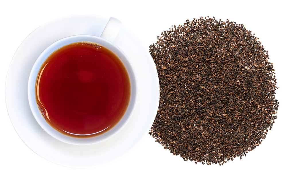 Tasse schwarzer Tee neben losen Teeblättern