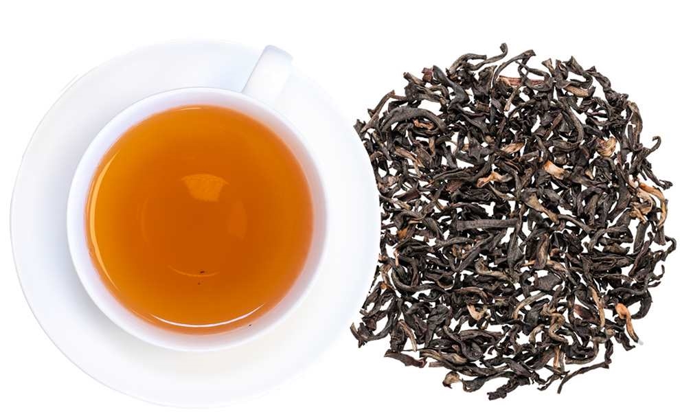 Weiße Tasse mit schwarzem Tee und losem Blatttee