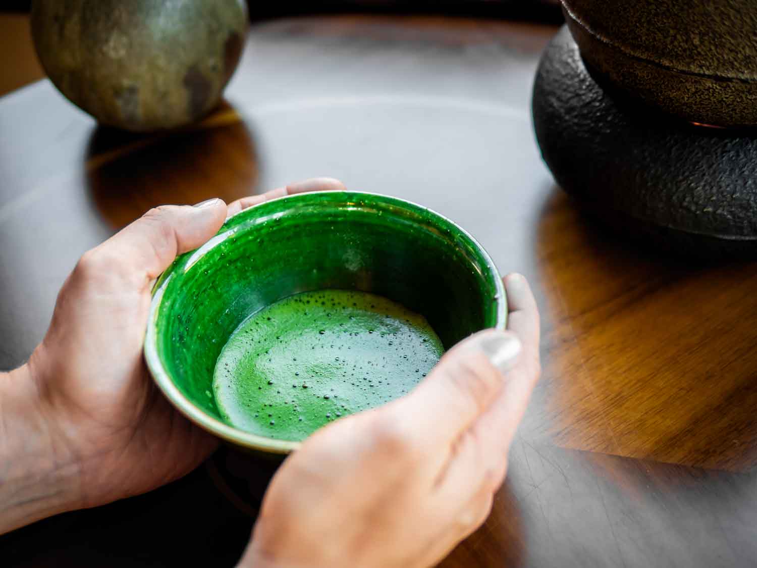 Hände halten grüne Schale mit Matcha-Tee