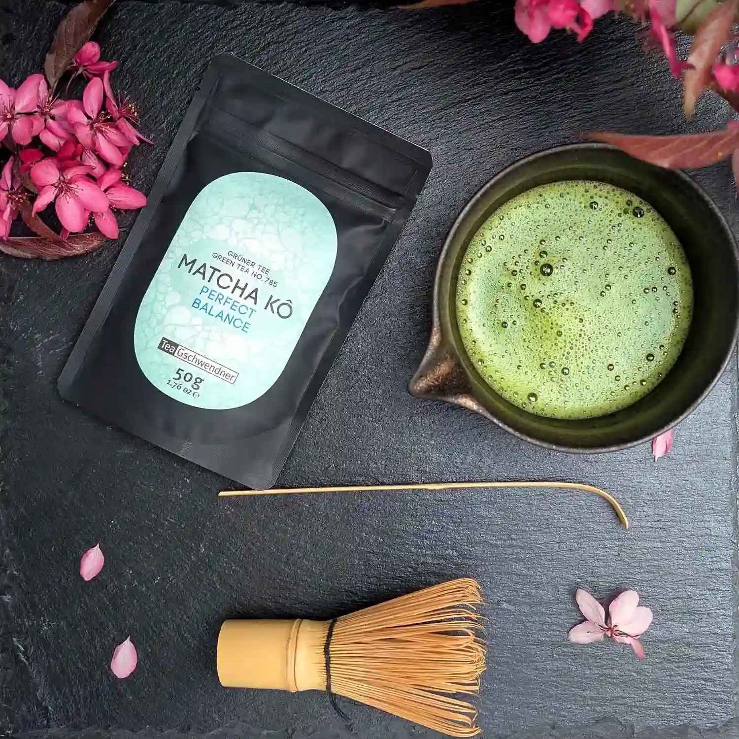 Japan Matcha Kô "Perfect Balance" in a 50 g pouch beside a frothy matcha bowl and bamboo whisk – balanced Japanese matcha for pure enjoyment, lattes and desserts