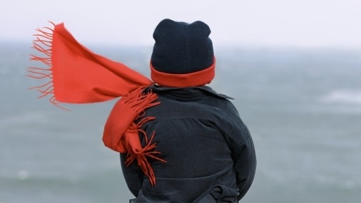 Junge mit Winterjacke und rotem Schal und Mütze von hinten fotografiert