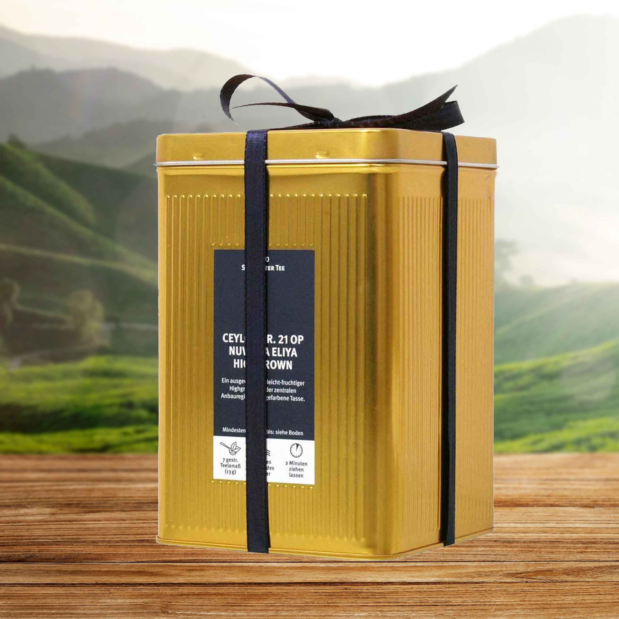 Goldene Teedose mit Schleife auf Holztisch vor Teefeld, tee tin, gold tin, gift box, metal container, ribbon wrap