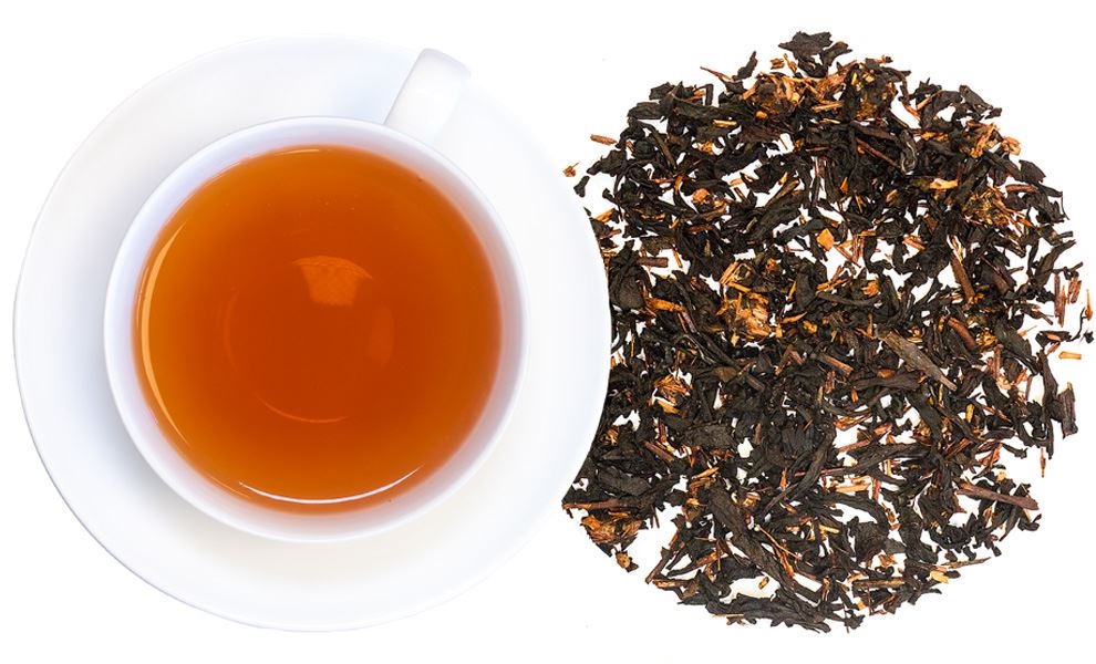 Weiße Tasse mit aufgebrühtem Schwarztee und losem Blatttee, tee, schwarztee, tee-blätter, braune tasse, orange-braune Flüssigkeit