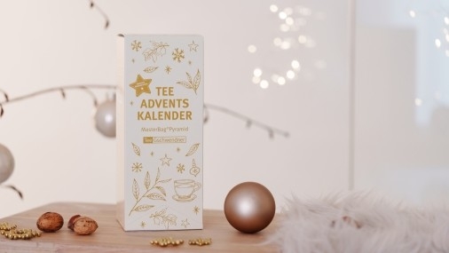 Hochkant-Kartonschachtel eines Tee-Adventskalenders auf einem Holztisch mit weihnachtlicher Deko