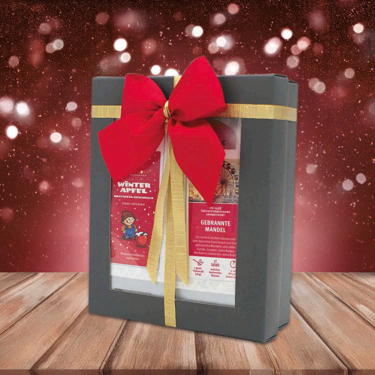 Beautiful gift box with red ribbon, contains winter flavours Baked Apple and Roasted Almond on wooden table against festive background
