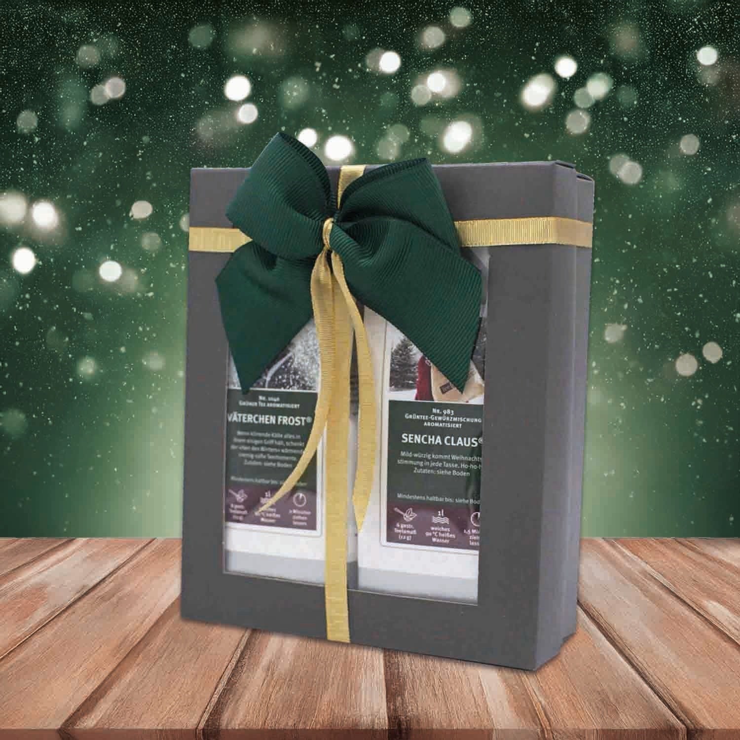 Gift-wrapped Christmas tea set with green and gold bow on a wooden table, snow in the background