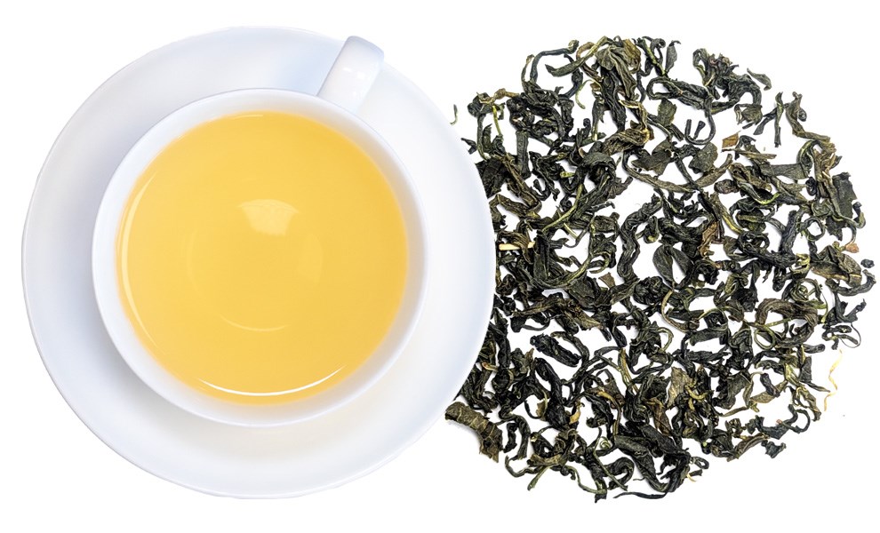 Tasse blanche avec thé vert jaune clair à côté de feuilles de thé vert en vrac sur fond blanc