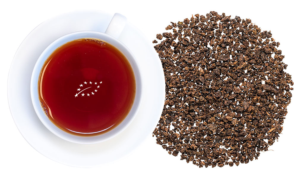 Weiße Tasse mit Schwarzem Tee und losem Tee daneben