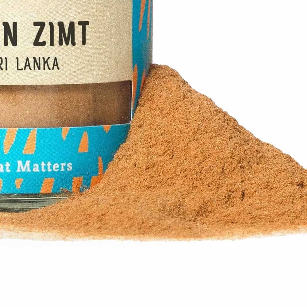 Glass jar filled with ground Ceylon cinnamon from Sri Lanka next to a pile of cinnamon powder