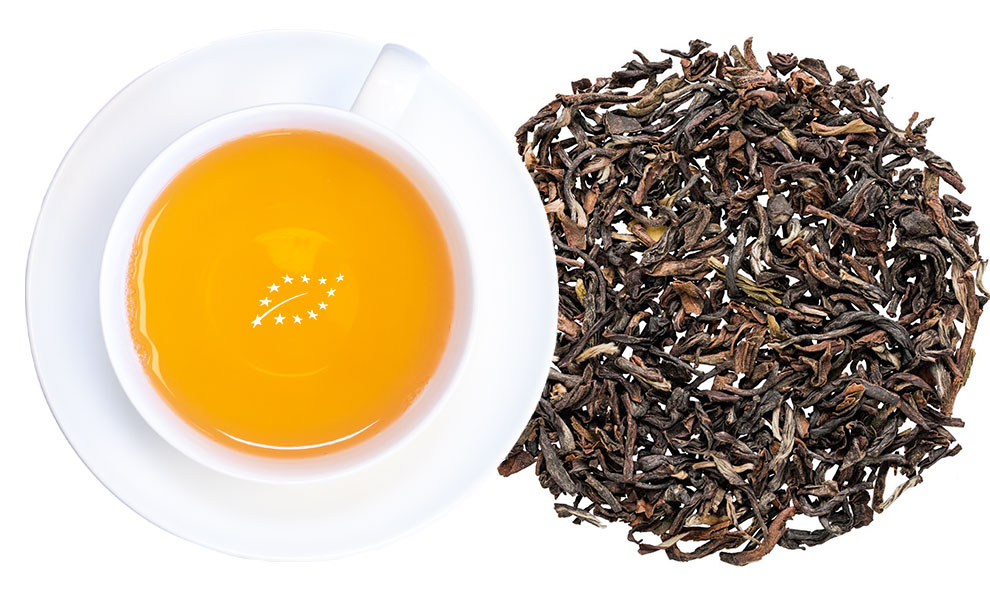 Weiße Tasse Schwarztee neben losen Teeblättern