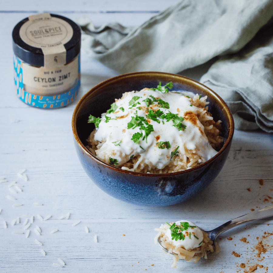 Bol en céramique avec riz assaisonné, yaourt crémeux, herbes fraîches et SoulSpice cannelle de Ceylan sur table en bois clair