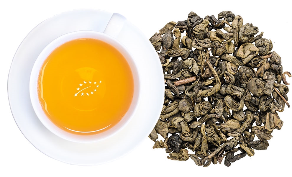 Weiße Tasse mit aufgegossenem grünem Tee und losen Blättern, tee, tea cup, tea leaves, herbal tea, orange brew