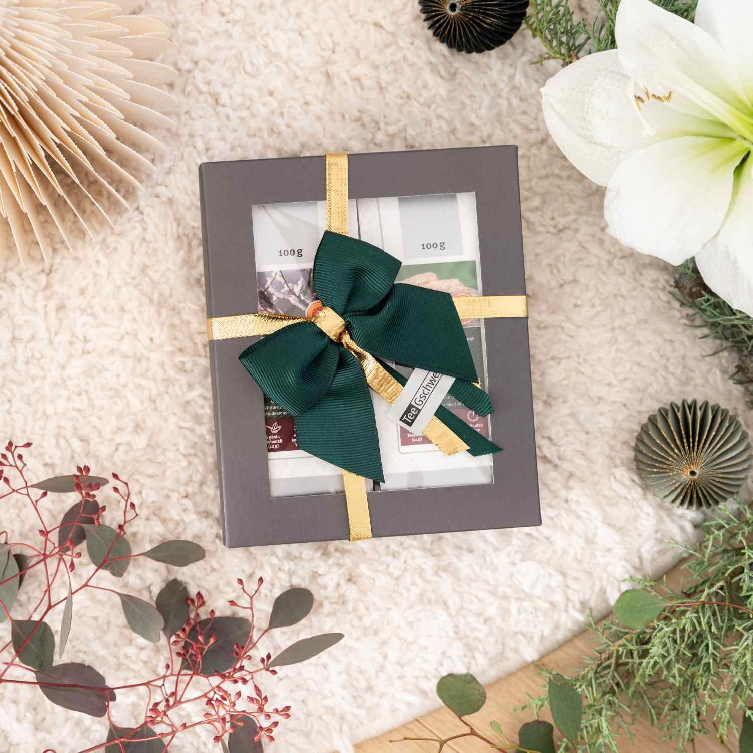 Geschenkbox mit Tee und grüner Schleife auf Deko-Untergrund, Geschenkbox, Dekorationsbox, grüne Schleife, goldenes Band, Geschenkverpackung
