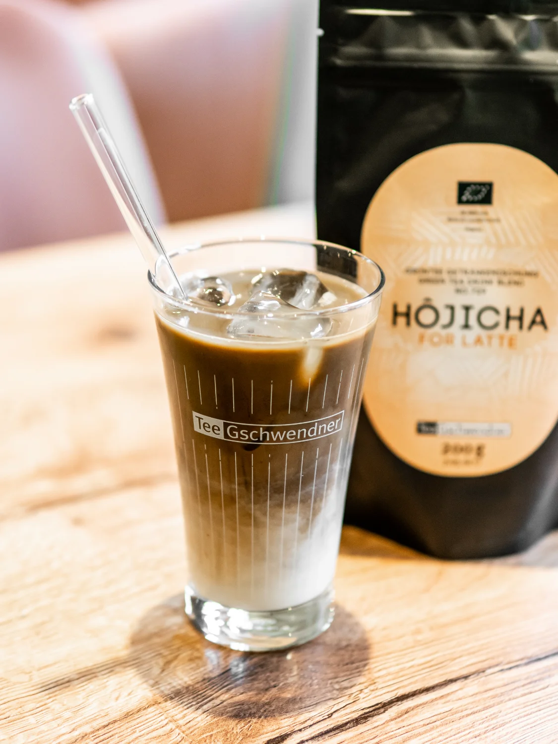 Glas Iced Hōjicha Latte mit Eiswürfeln auf Holztisch