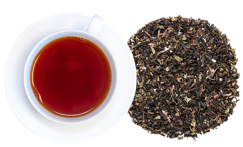 Weiße Tasse mit schwarzem Tee und losem Tee daneben