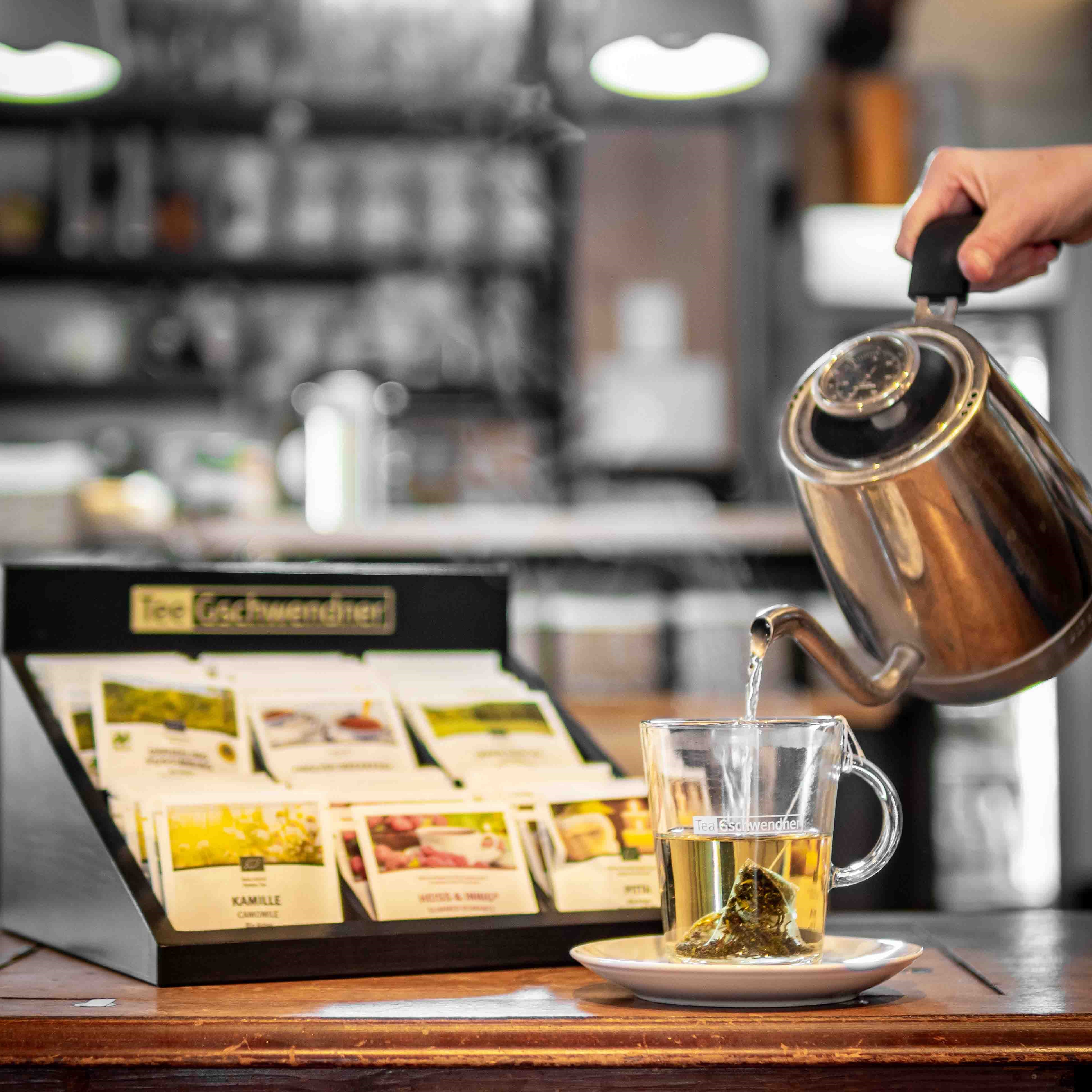 Teebeutel im Glas, heißes Wasser aus Kanne wird eingeschenkt, Kaffeethe, Teebeutel, Teekanne, Glasbecher, Wassertemperatur