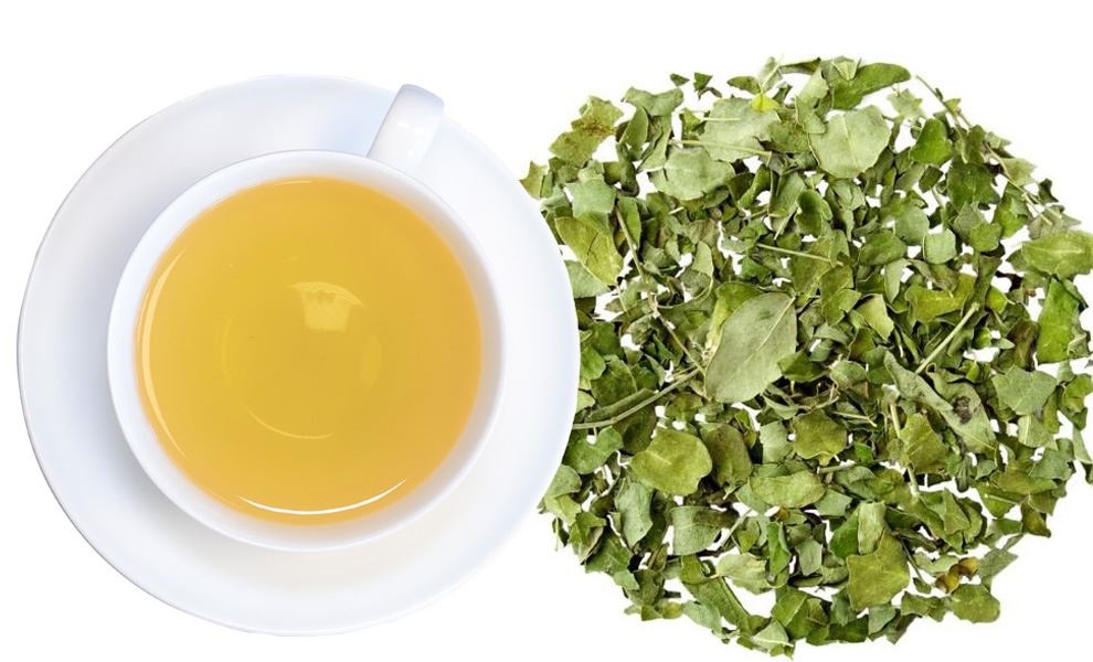 Weiße Tasse Kräutertee neben getrockneten Blättern, tee, tee-setup, kräutertee, getrocknete-kräuter, grüner-tee-blätter