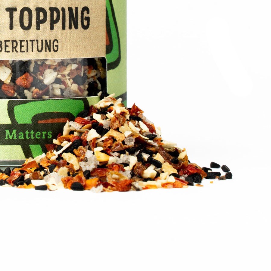 Open jar with colourful seasoning topping mix spilling decoratively onto a white surface