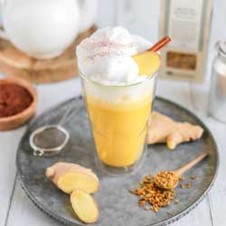 Ingwer-Honig-Latte in Glas mit Schaum, Ingwer und Gewürzen a