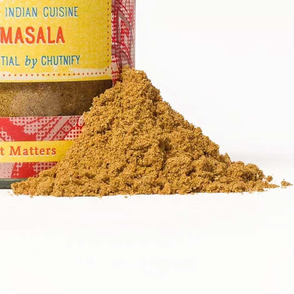 Tas de poudre d’épice garam masala devant un bocal d’épices coloré