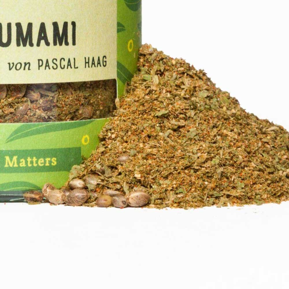 Gros plan sur une boîte ouverte contenant un mélange d’épices umami de Pascal Haag, à côté d’un tas d’herbes et d’épices grossières