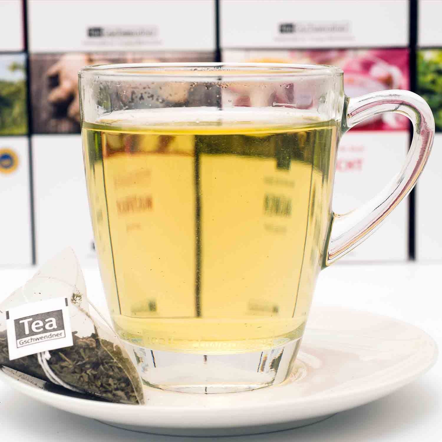Tasse mit grünem Tee und Pyramiden-Teebeutel auf Untertasse, tee, getränk, glas, heiße-getränke, tea-gift-set