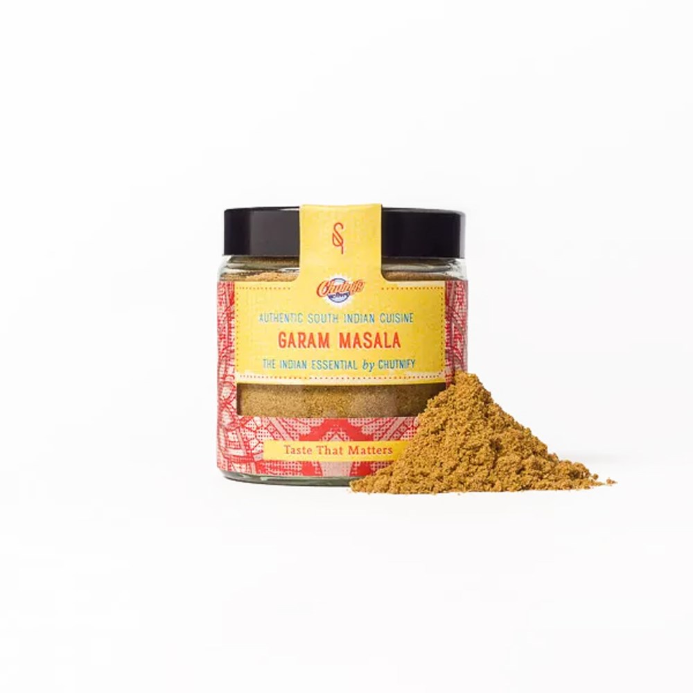 Bocal de mélange d’épices Garam Masala avec un petit tas d’épice moulue à côté sur fond blanc
