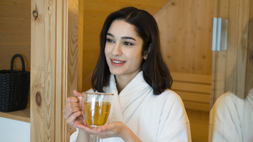 Junge Frau mit dunklen Haaren im Bademantel beim Teetrinken