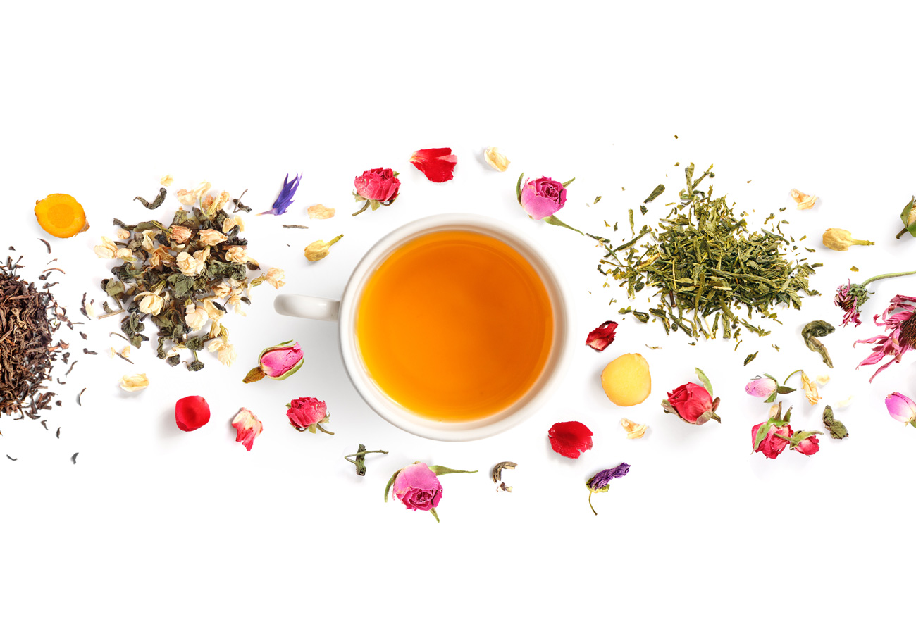 Tasse mit Tee und verschiedene Teeblätter sowie Blüten auf w