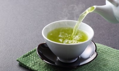 Produktbild: Frisch aufgegossener grüner Tee in weißer Tasse auf schwarzer Untertasse, serviert auf grünem Platzset