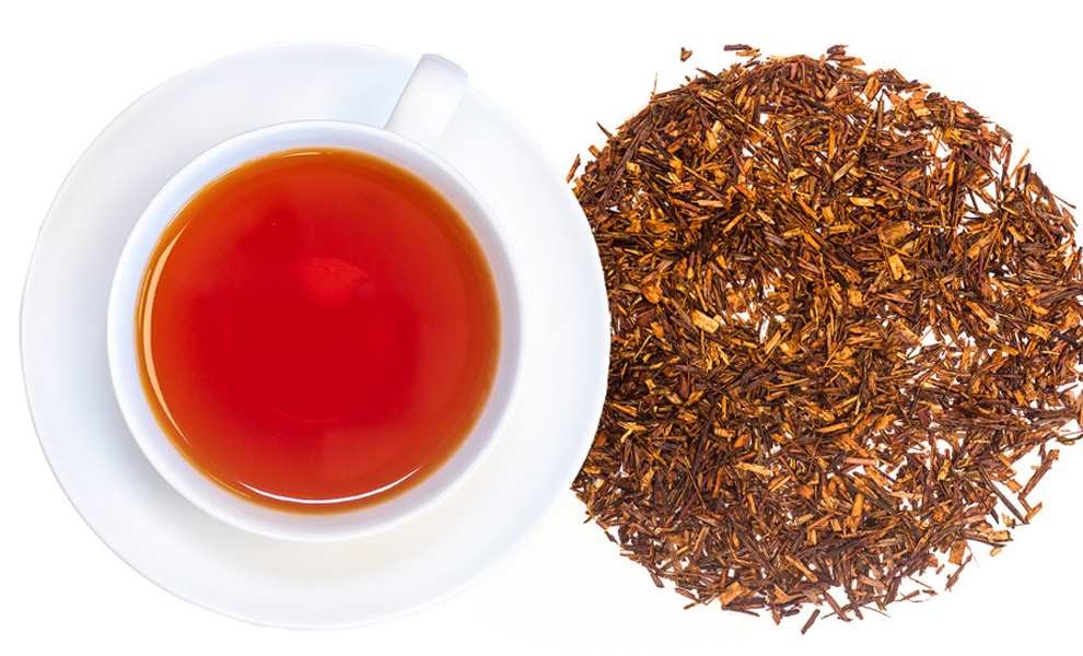 Weiße Tasse mit Rooibostee und losem Rooibostee daneben, tee, tee blätter, kupferrot, rohrzucker?, kiefer?