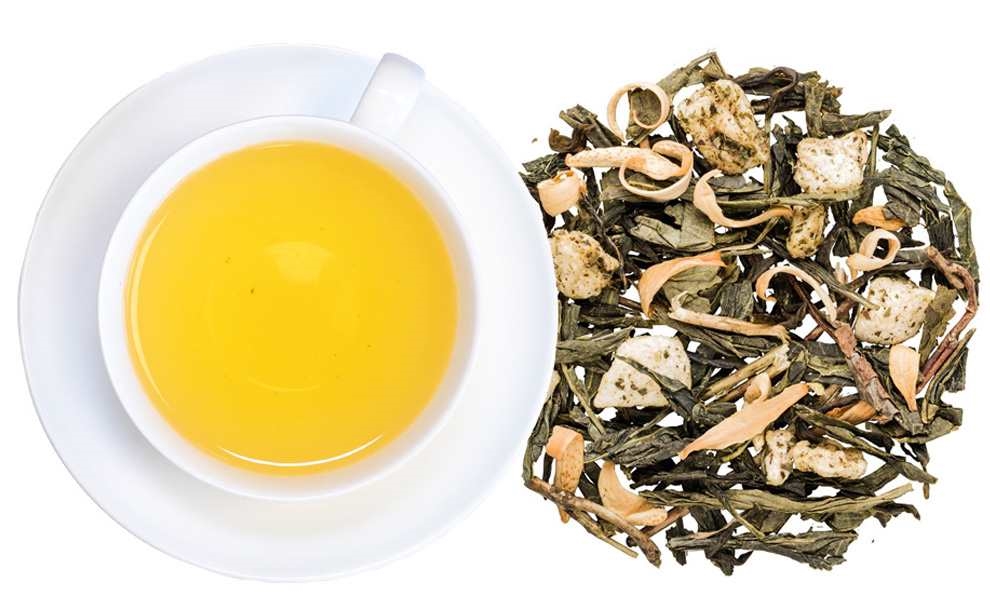 Weiße Tasse mit aufgebrühtem grünem Tee und losem Blatttee, grüner tee, tee-blätter, loser tee, tee-infusion, gelbe flüssigkeit