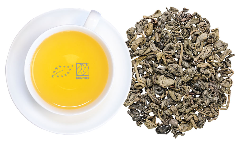Tasse grüner Tee neben losen grünen Teeblättern