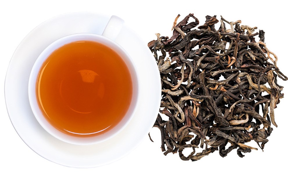 White cup of black tea next to loose tea leaves on white bac