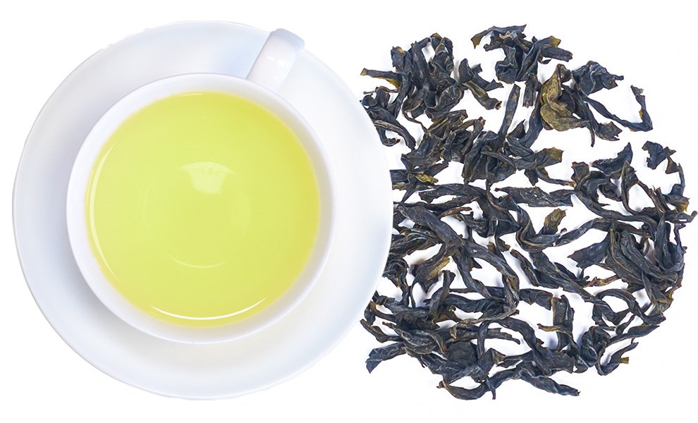 Weiße Tasse mit gelblich hellem Tee und daneben lose, dunkle Teeblätter als Produktansicht