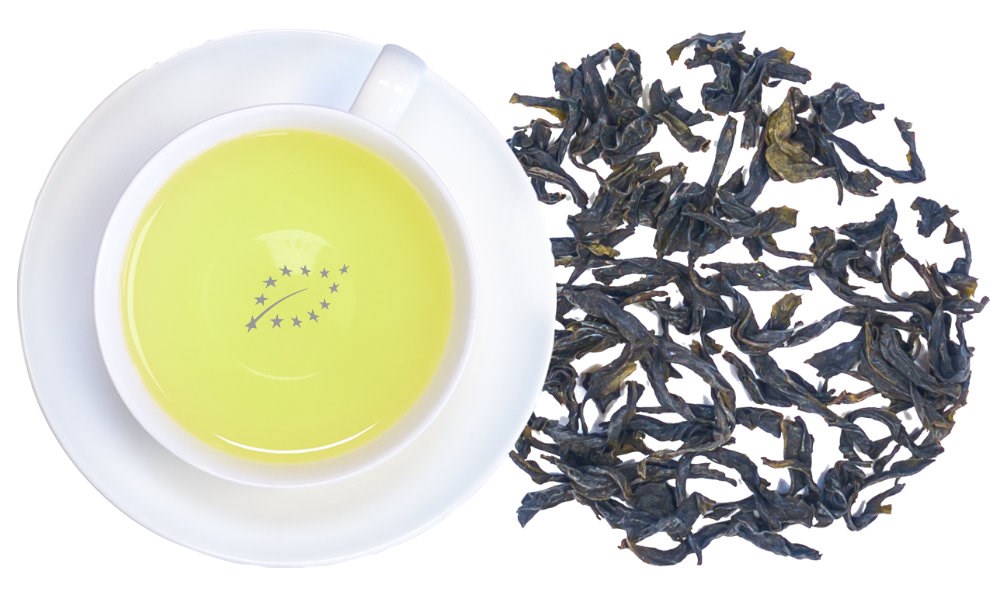Weiße Tasse mit gelblich hellem Tee und daneben lose, dunkle Teeblätter als Produktansicht, grüner Tee, Tee-Blatt, Europäischer Tee, Tee-Blätter, gelber Tee