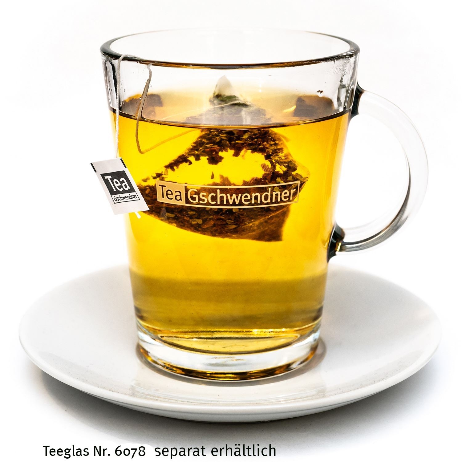 Klares Teeglas mit Tee und Beutel auf weißem Teller, Tee, Kräutertee, Glasbecher, Teebeutel, Goldenes Bernstein