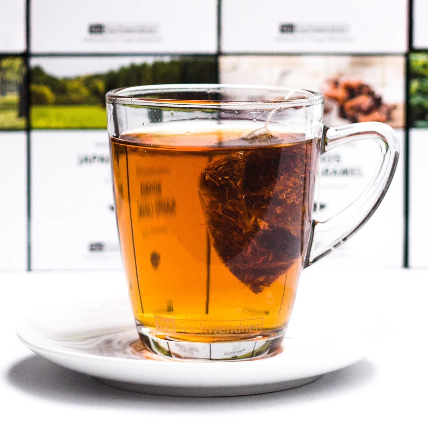 Heißer Tee im Glas mit Teebeutel auf weißem Teller, Tee, Teeglas, Klartee, Teestück, Teezubereitung