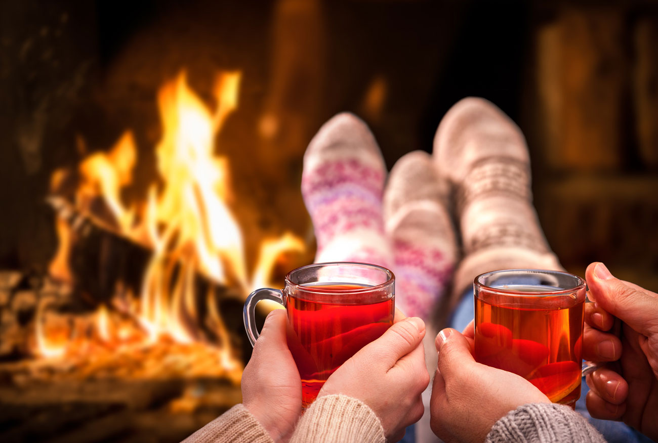 Zwei Personen mit Wollsocken trinken Tee vor dem Kamin