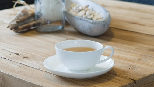 Weiße Teetasse mi goldgelbem Tee auf einem Holztisch