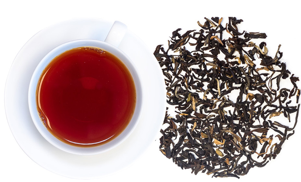 Weiße Tasse mit schwarzem Tee und losen Teeblättern
