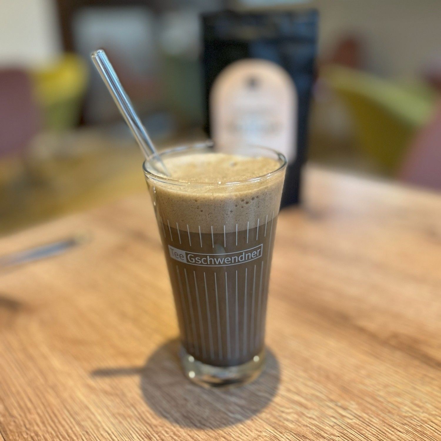 A glass of frothy iced coffee with a straw on a table
