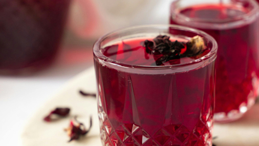 dunkelroter Tee in einem Glas mit getrockneten Hibiskusblüten