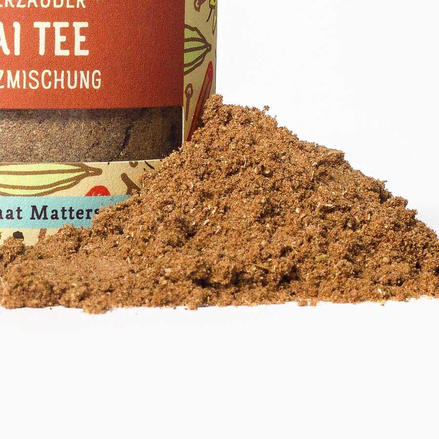 Close-up of an aromatic chai tea spice blend in a glass jar with loose powder in the foreground