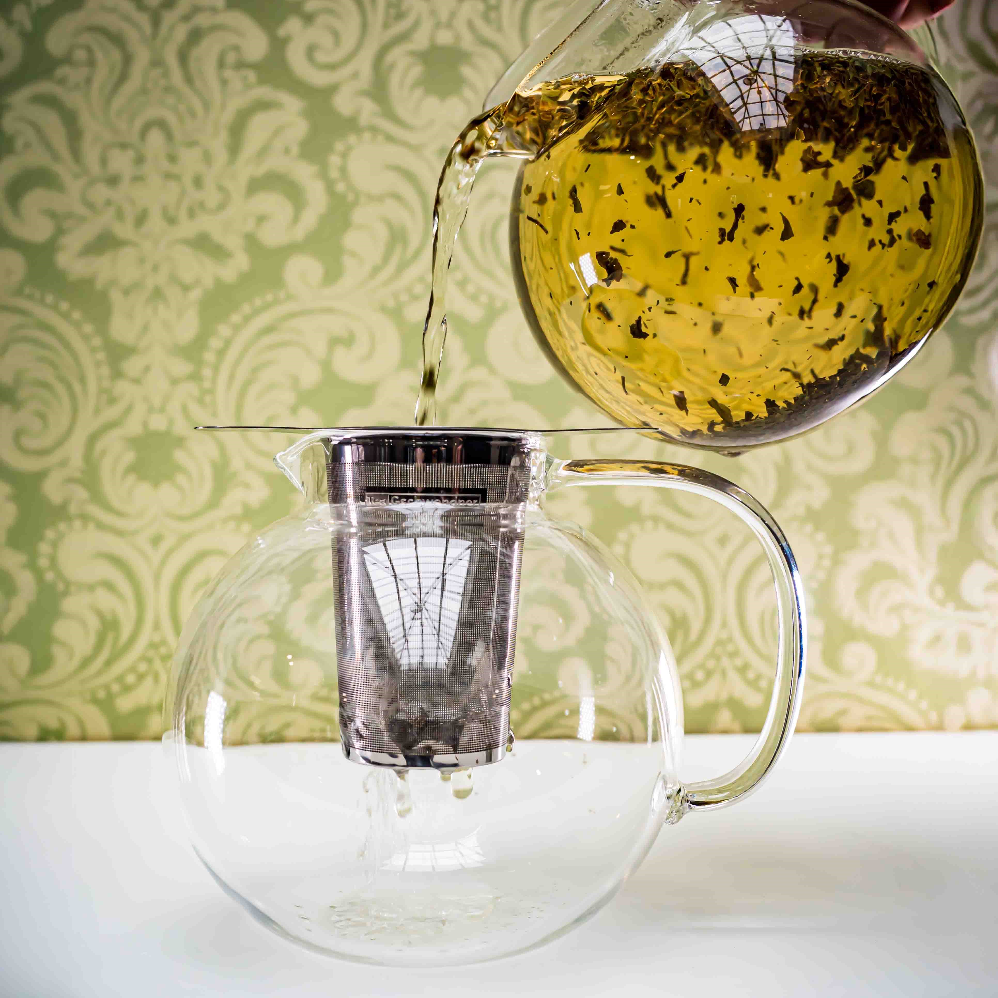 Heißer Tee wird in Glasteekanne mit Sieb gegossen, Glaskanne, Kaffeekanne, Teekanne, Teekanne-Filter, Teekocher