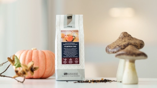 Teetüte mit Pumpkin Chai Tee auf einem hellen Untergrund, daneben stehen Dekopilze und ein Dekokürbis