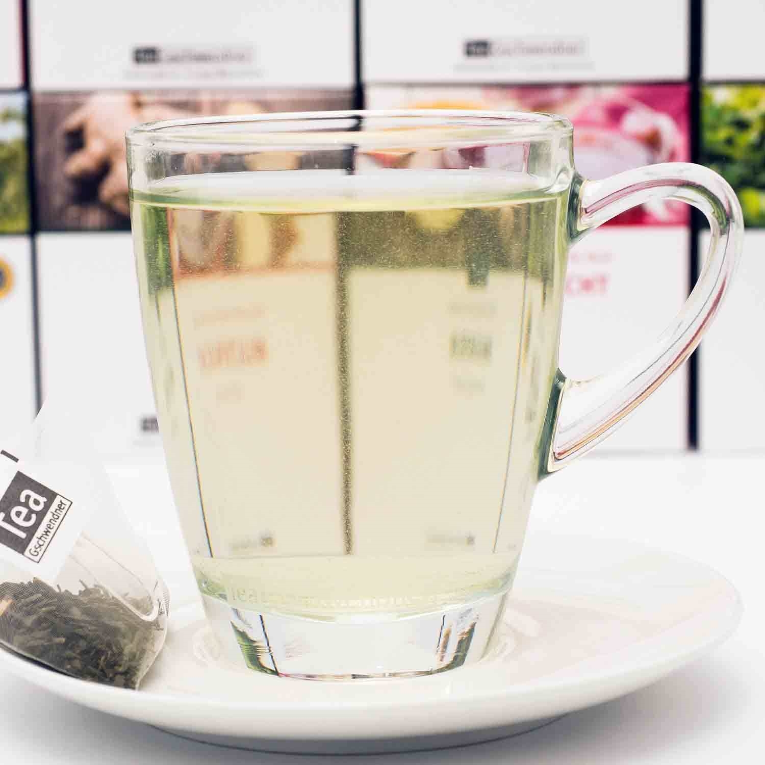 Heißer grüner Tee im Glas mit Teebeutel auf Untertasse, glas, tee, heißgetränk, becher, infusion