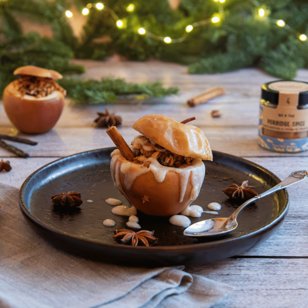 Close-up of a festive baked apple with nut filling, cinnamon sauce and star anise on a black plate with Christmas decorations in the background