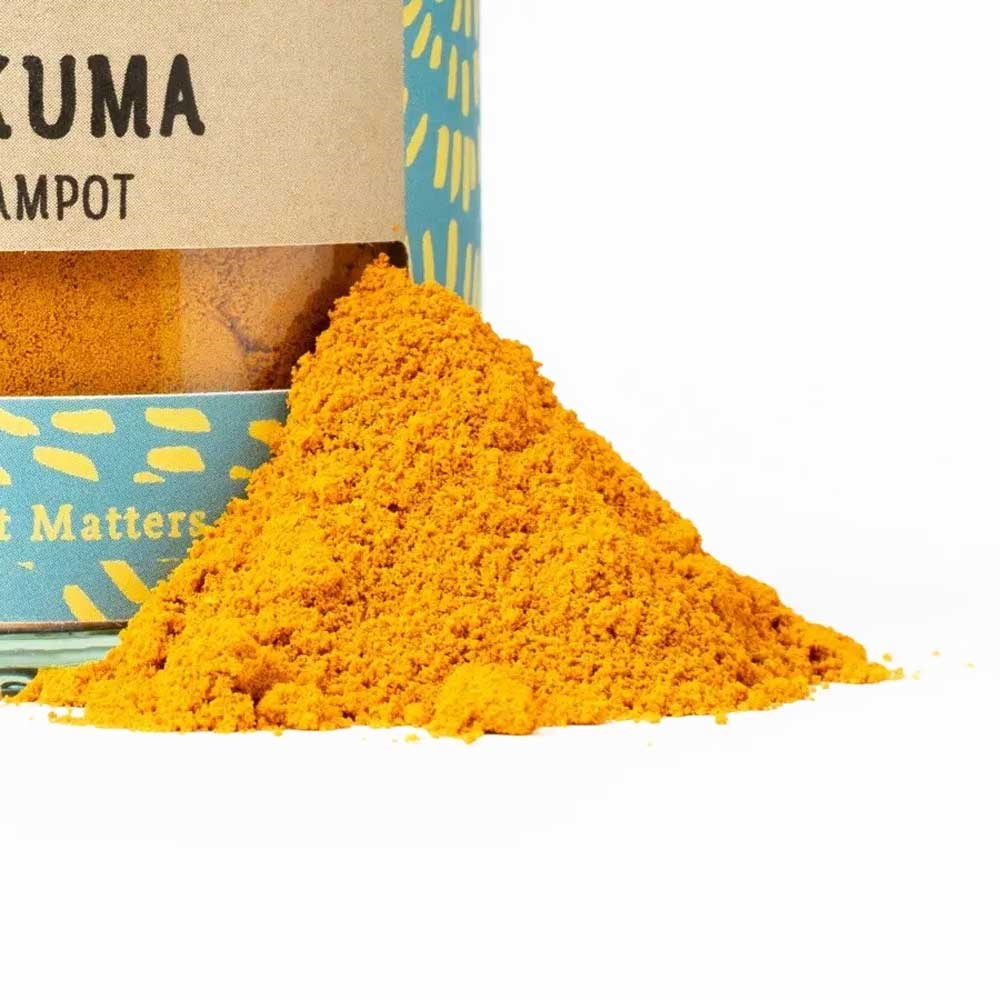 Poudre de curcuma jaune vif devant une boîte décorative remplie de curcuma moulu